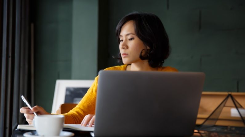 young business woman in yellow dress sitting at table in cafe and writing in notebook student t20 9lPGJN